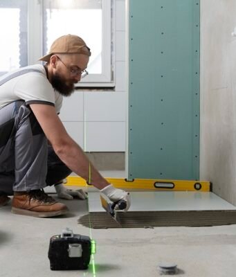 Koliko košta renoviranje vodovodne instalacije u kupatilu? Majstor postavlja pločice tokom renoviranja kupatila